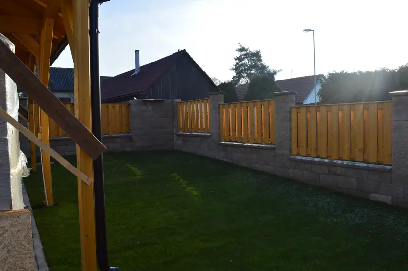 Dřevěný laťkový plot mezi zděnými sloupky na zahradě